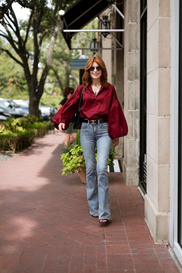 woman wearing one of the Best tops for Women Over 50 from Harshman wine coloured blouse, jeans, and Chanel belt