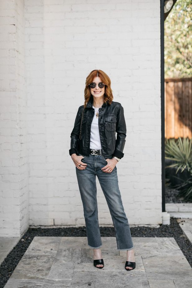 Over 50 fashion influencer wearing straight leg denim with black mules and coated denim jacket with white tee.
